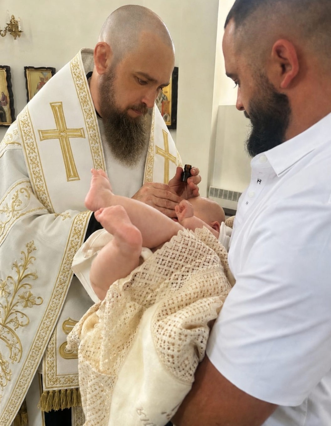 Vladika Herman, Obispo de Pechersk, unge al infante con el óleo bendecido antes de la inmersión bautismal, como signo de preparación para participar sacramentalmente en la muerte y resurrección de Cristo.